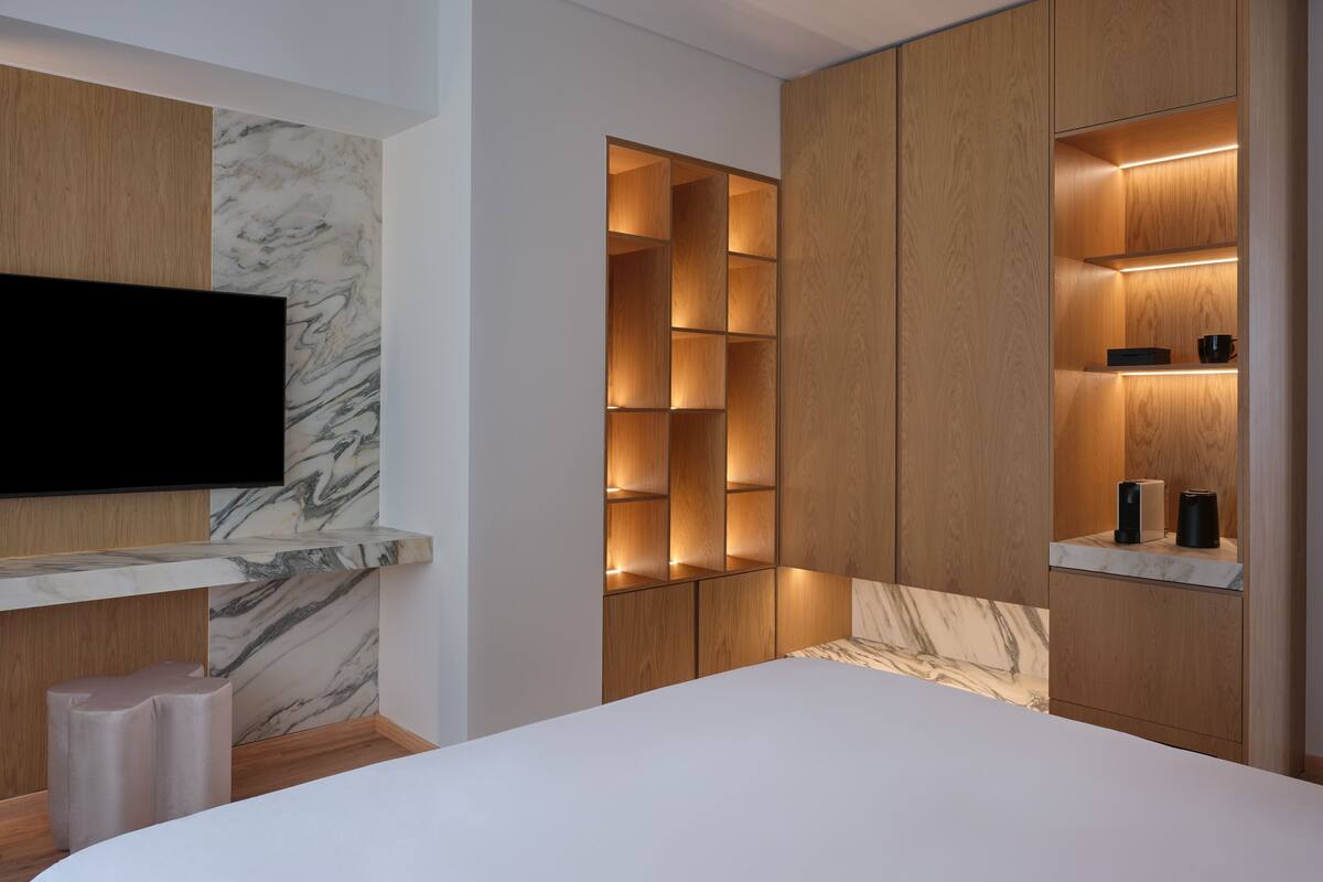 Ein modernes Schlafzimmer mit einem großen Bett, eingebauten Holzbögen, einem Flachbildfernseher und Marmor-Akzenten.