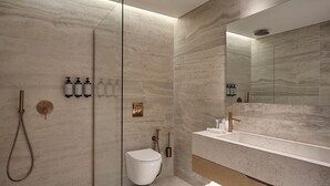 A modern bathroom with a glass-enclosed shower, a white toilet, and a large mirror above a sink with a wooden countertop. - Nur City Suites (Athens)
