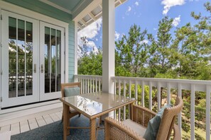 A covered porch with a glass table and wicker chairs, overlooking a forested area. - Aquamarine in The Preserve at Grayton - Included Golf Cart, Close to Pool! (Santa Rosa Beach)