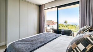 Hotellihuone, jossa on suuri sänky, merinäköala ja parveke, jossa on ulkokalusteita.