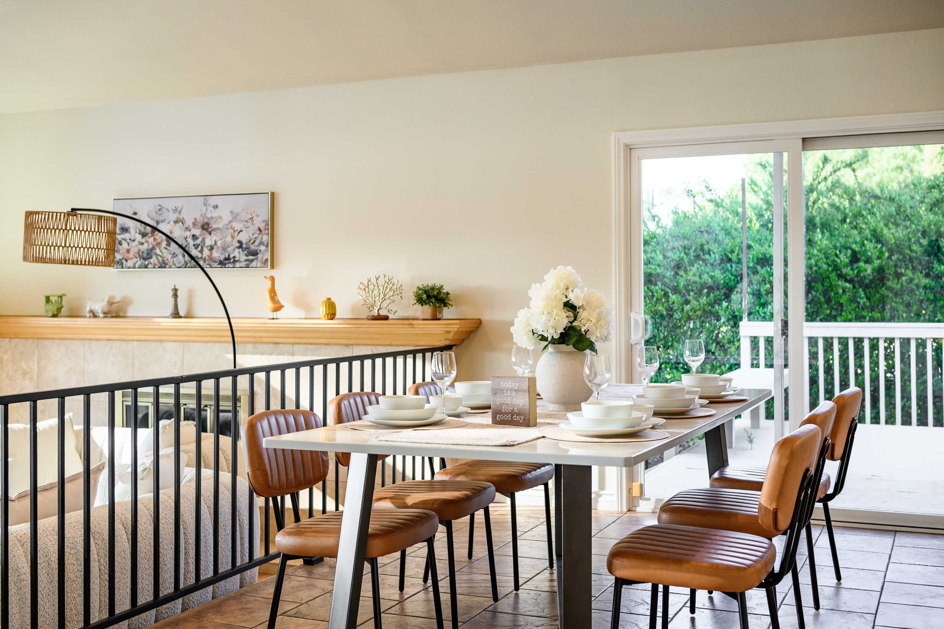 Un coin repas avec une longue table dressée pour quatre personnes, entourée de chaises, et offrant une vue sur la verdure à l’extérieur.