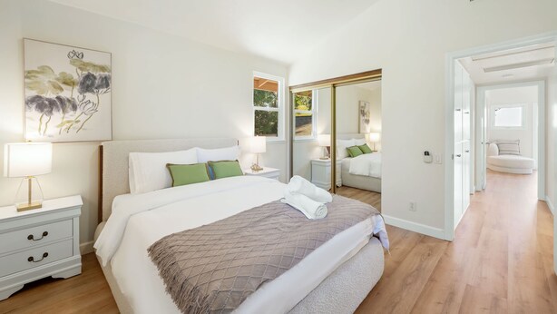 Een slaapkamer met een groot bed, nachtkastjes, een spiegel en een schilderij aan de muur.