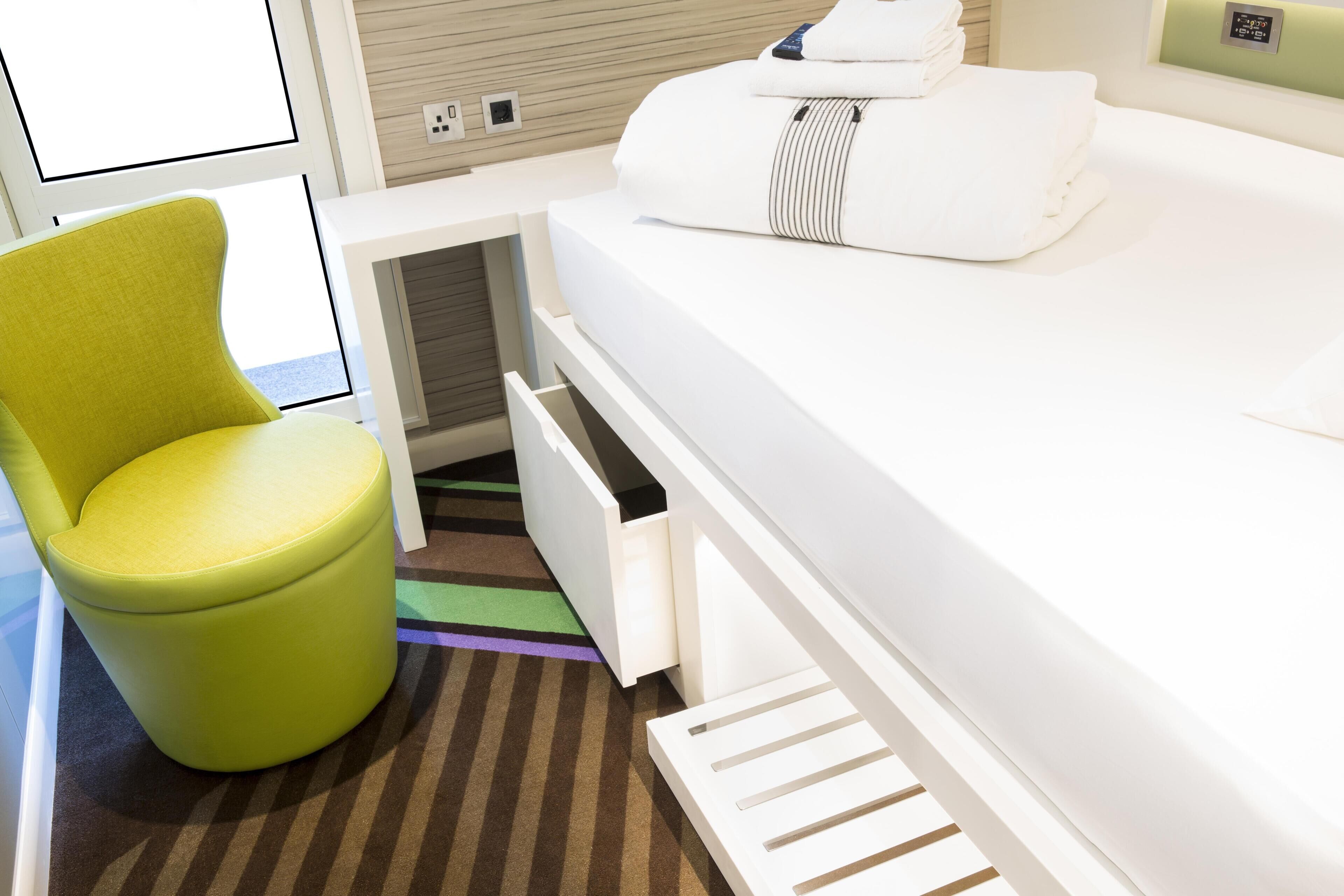 A compact room with a bed, a green chair, and a small storage space.