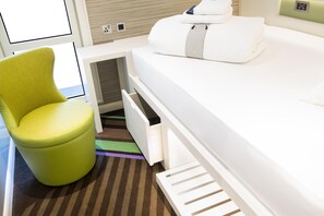 A compact room with a bed, a green chair, and a small storage space. - Hub By Premier Inn Edinburgh - Royal Mile (Edinburgh)