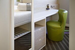 Un lit superposé avec un bureau et une chaise, une petite poubelle et une prise de courant.