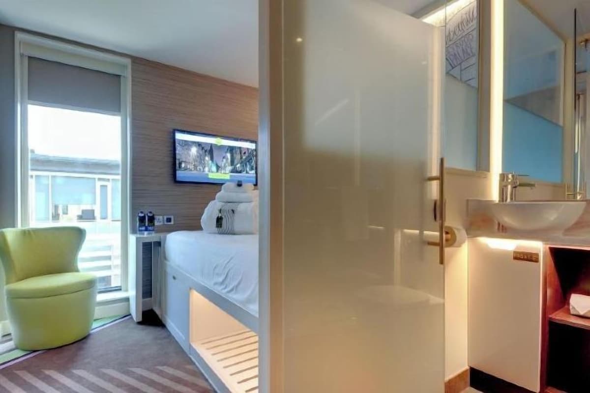 Une chambre d’hôtel comprenant un lit, un téléviseur fixé au mur, une salle de bain avec un lavabo et une chaise.