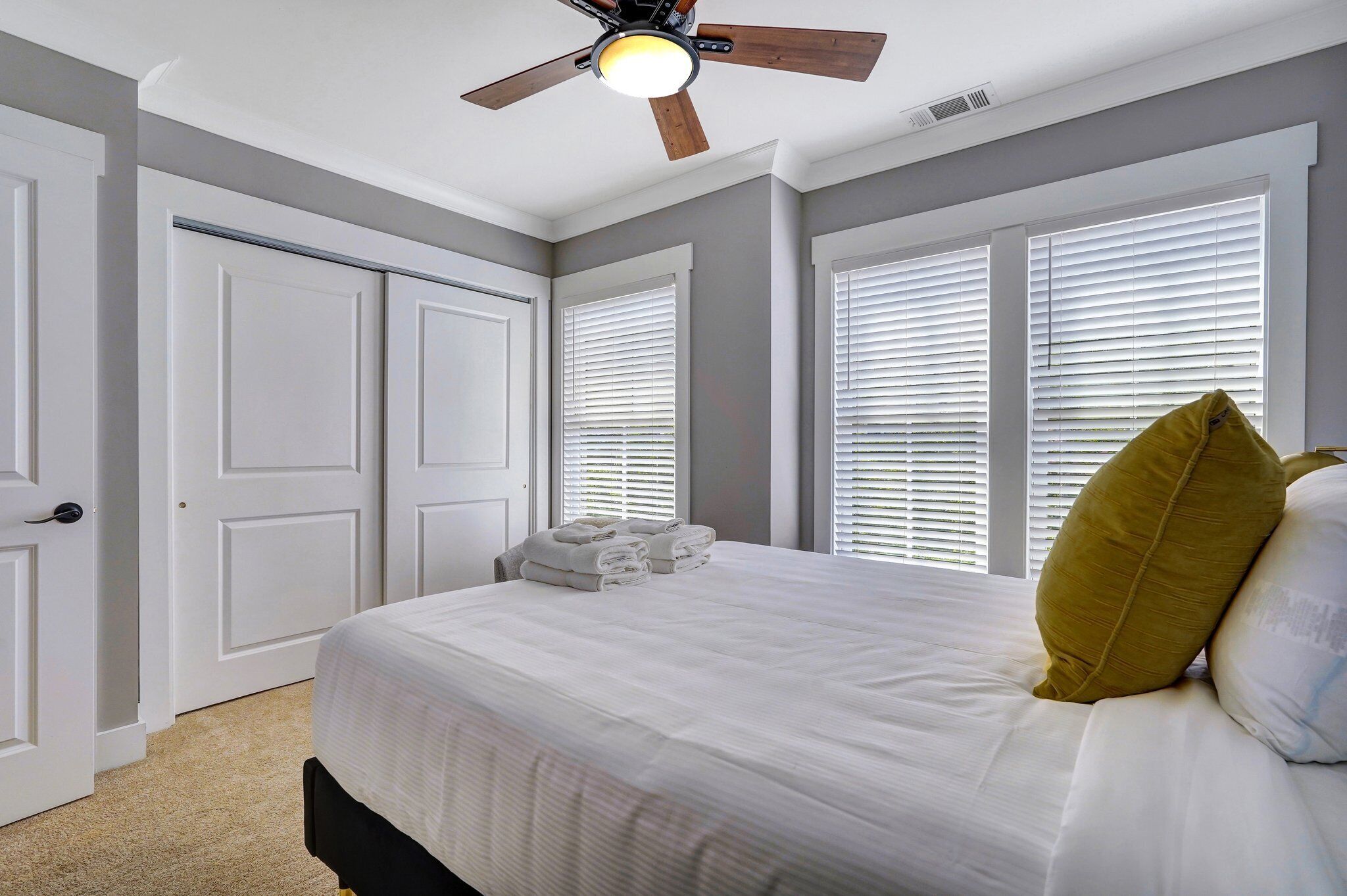 A bedroom with a bed, white curtains, a ceiling fan, and a door.