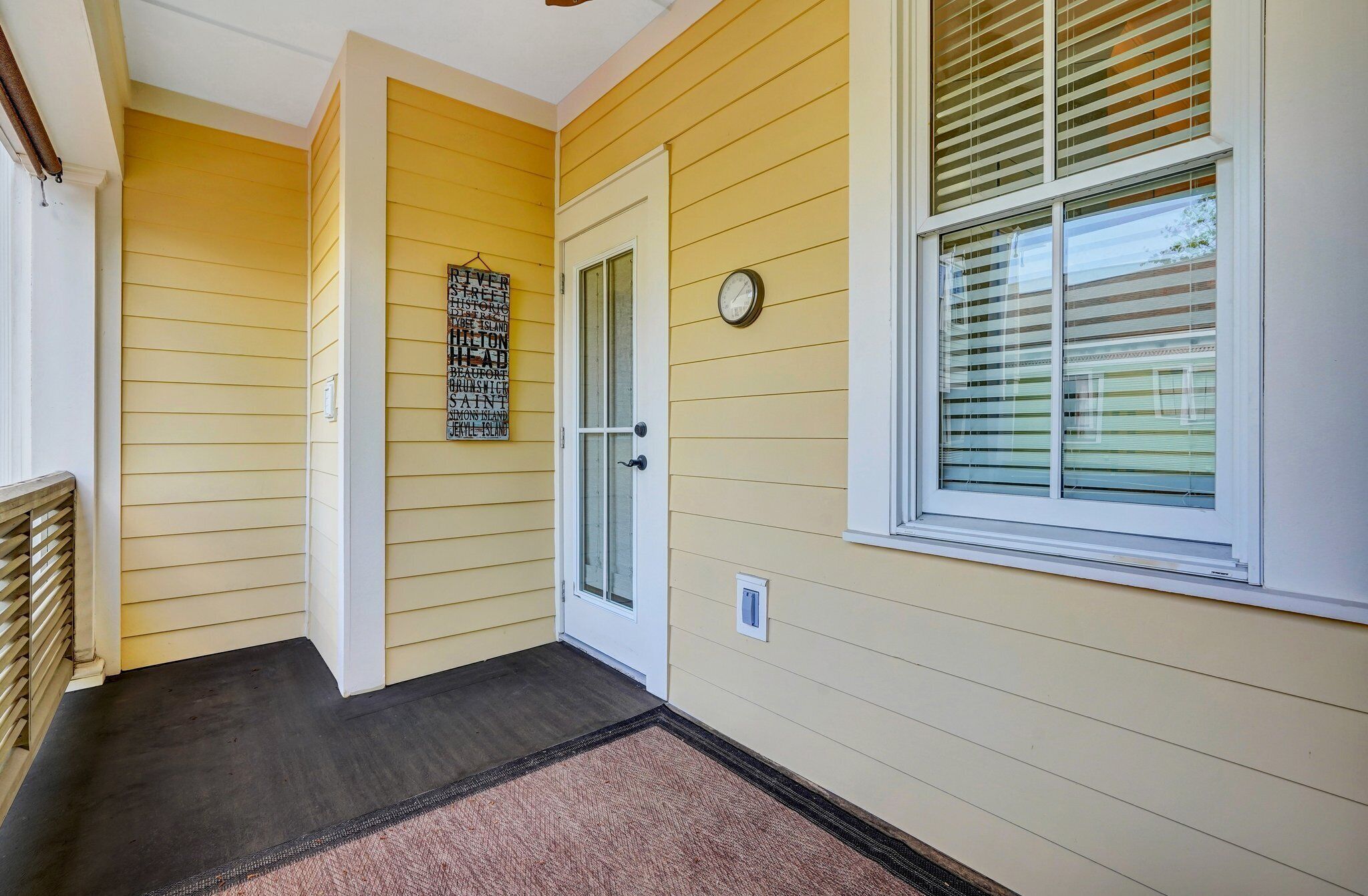A hallway with yellow siding, a door, a window with blinds, and a wall-mounted clock.