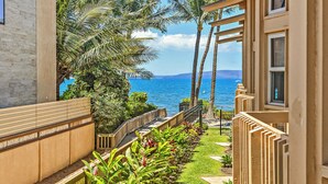 Un sendero conduce a un balcón con vistas al océano, rodeado de plantas tropicales y una valla de madera.