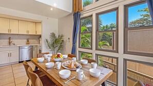 Una cocina moderna con armarios blancos, lavavajillas y comedor con mesa de madera lista para el desayuno.