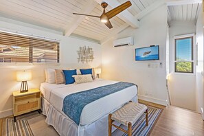 Een slaapkamer met een bed, nachtkastjes, een plafondventilator, een airconditioning, een televisie en een raam met zonwering.