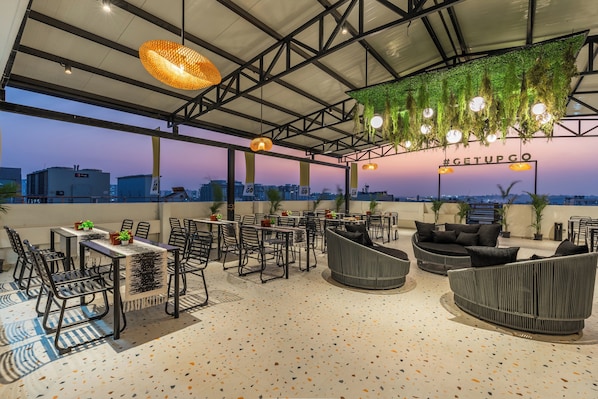 An outdoor seating area with tables and chairs, a view of the cityscape, and hanging greenery.