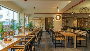 A spacious indoor area with multiple wooden tables and chairs, a pool table, and potted plants. - The Hosteller Bangalore, Marathahalli (Bengaluru)