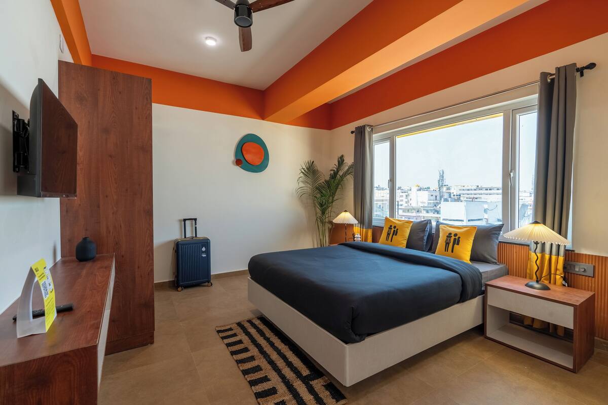 Ein modernes Hotelzimmer mit einem großen Bett, einem Schreibtisch, einem Koffer und Blick auf die Stadt.