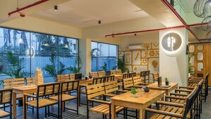 A modern cafe with wooden furniture, large windows, and a visible restroom sign. - The Hosteller Bangalore, Marathahalli (Bengaluru)