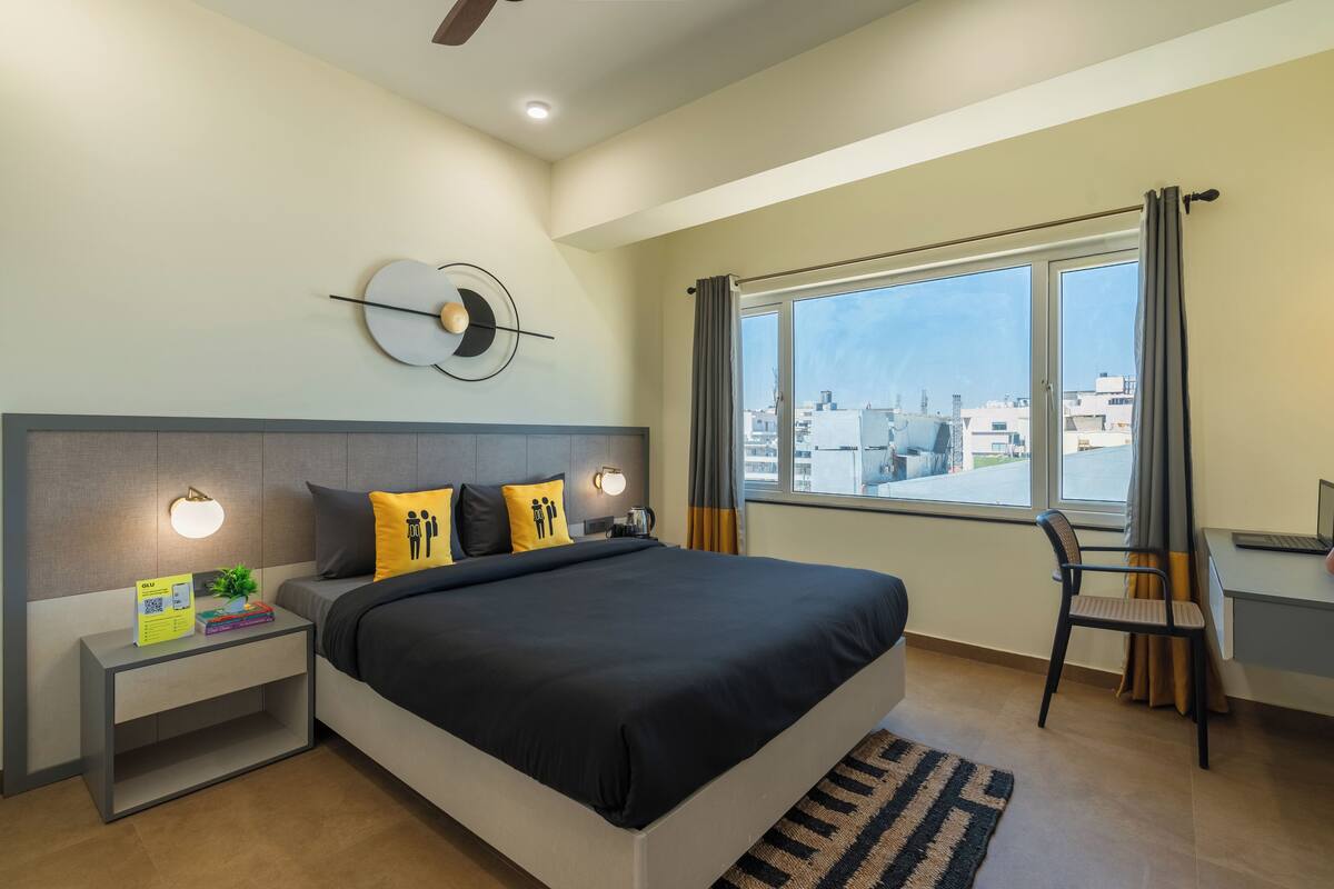 Ein modernes Schlafzimmer mit einem großen Bett, Nachttischen, einem Schreibtisch und Blick auf die Stadt.