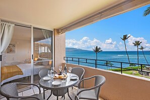 A balcony with a table set for dining, overlooking a beach with palm trees and the ocean.