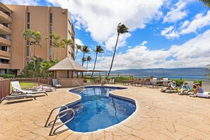 A pool area with lounge chairs, a small pool, and a view of the ocean.
