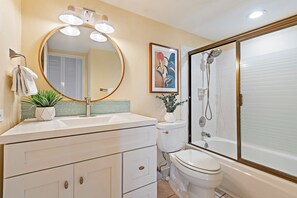 A bathroom with a round mirror, a sink, a toilet, and a shower.
