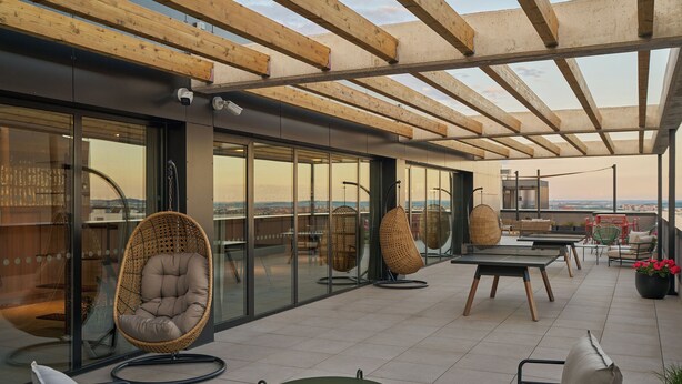 A rooftop terrace with glass walls, wooden beams, wicker chairs, and a table. - The Carabanchel Episode (Madrid)