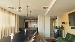 A modern kitchen with a dining area, featuring a long table, chairs, pendant lights, and a green sofa. - The Carabanchel Episode (Madrid)