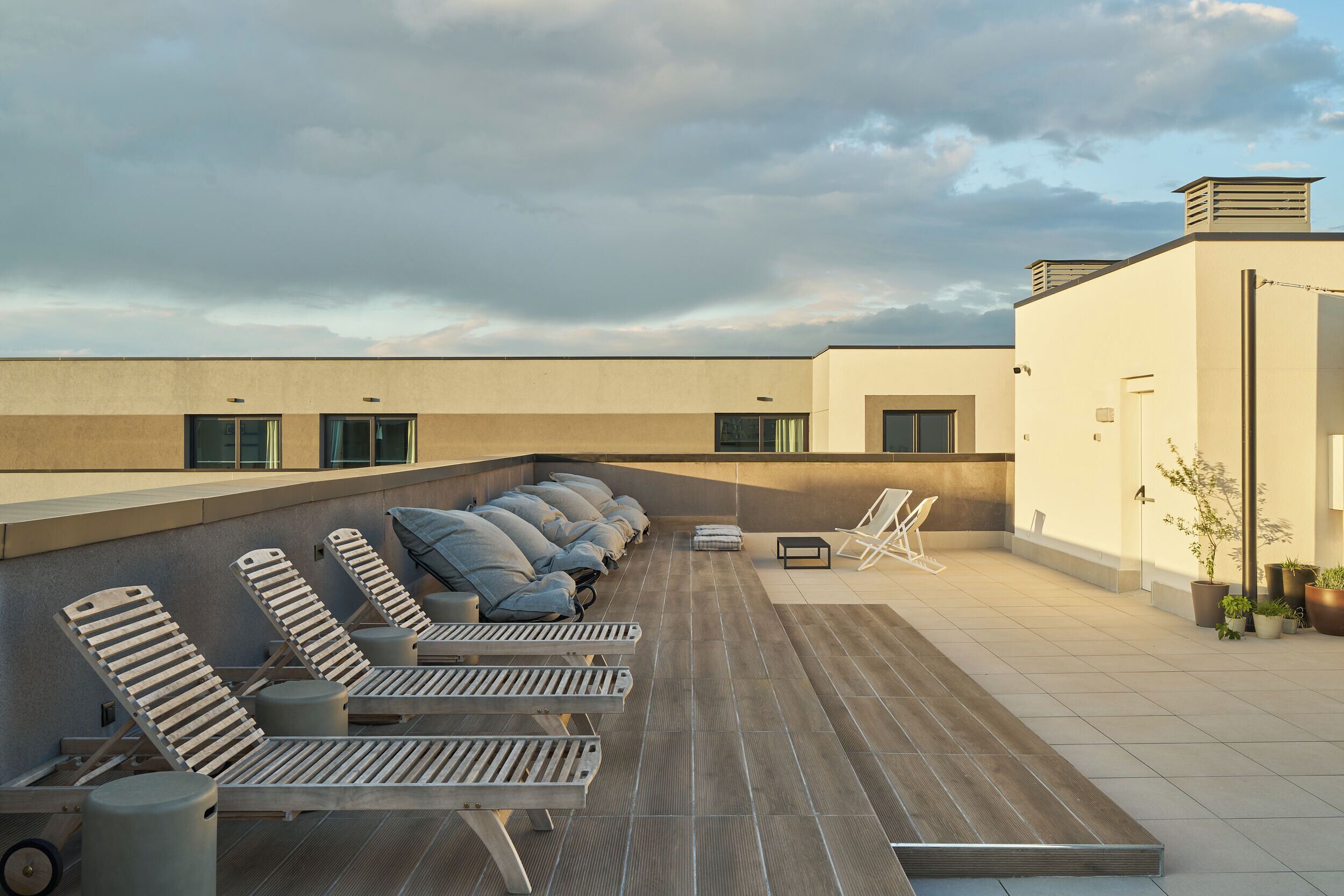 A rooftop terrace with sun loungers, a small table, and potted plants.