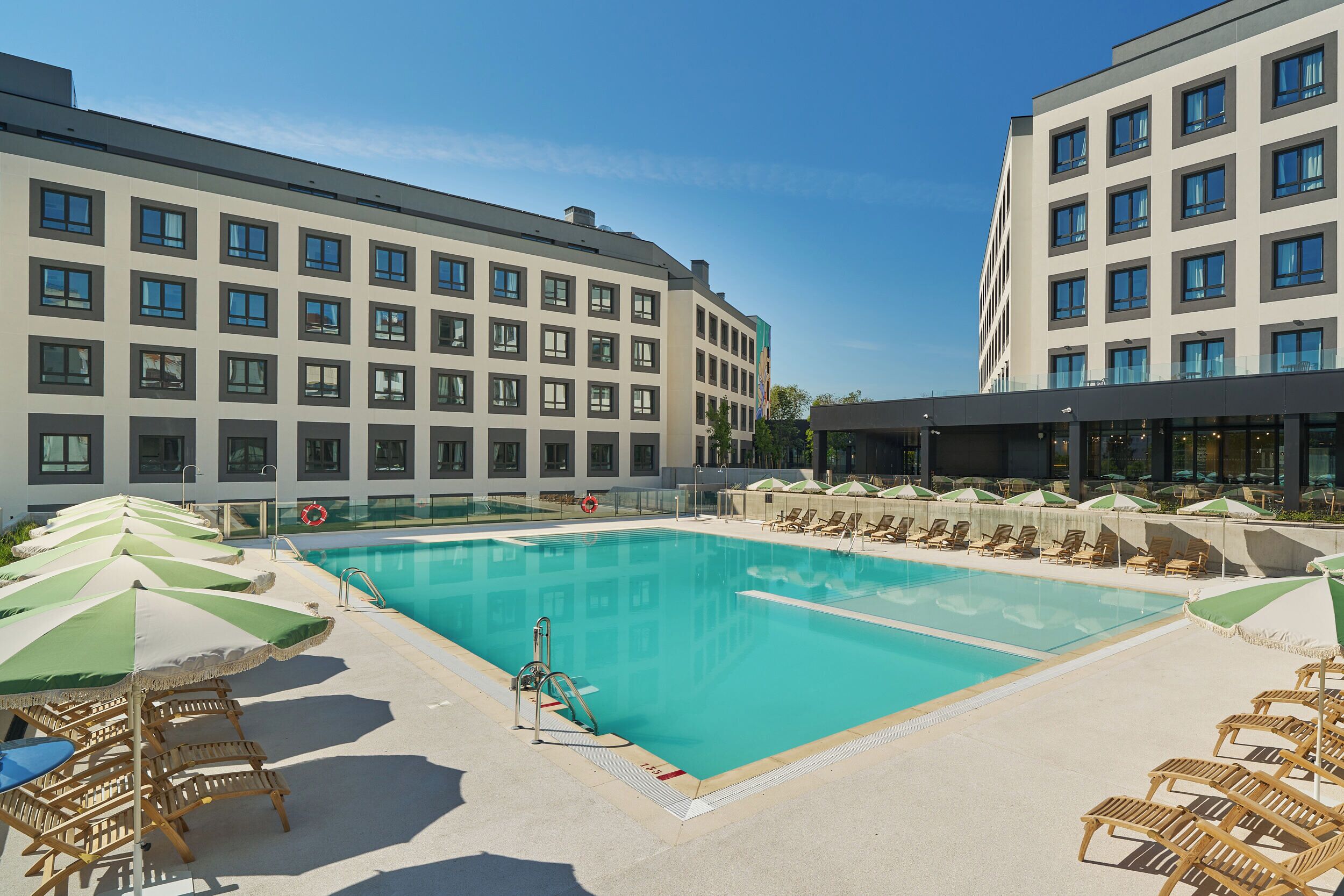 Ein Schwimmbecken mit Liegestühlen und Sonnenschirmen, umgeben von modernen Gebäuden.