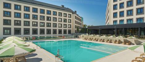 Ein Schwimmbecken mit Liegestühlen und Sonnenschirmen, umgeben von modernen Gebäuden.