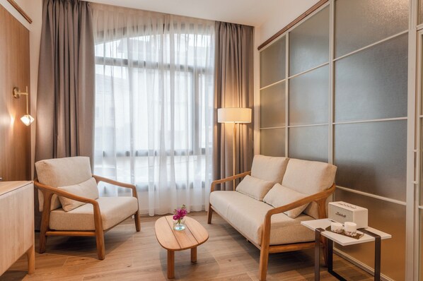 Una habitación de hotel moderna con dos sofás, una mesita, una lámpara y un minibar.