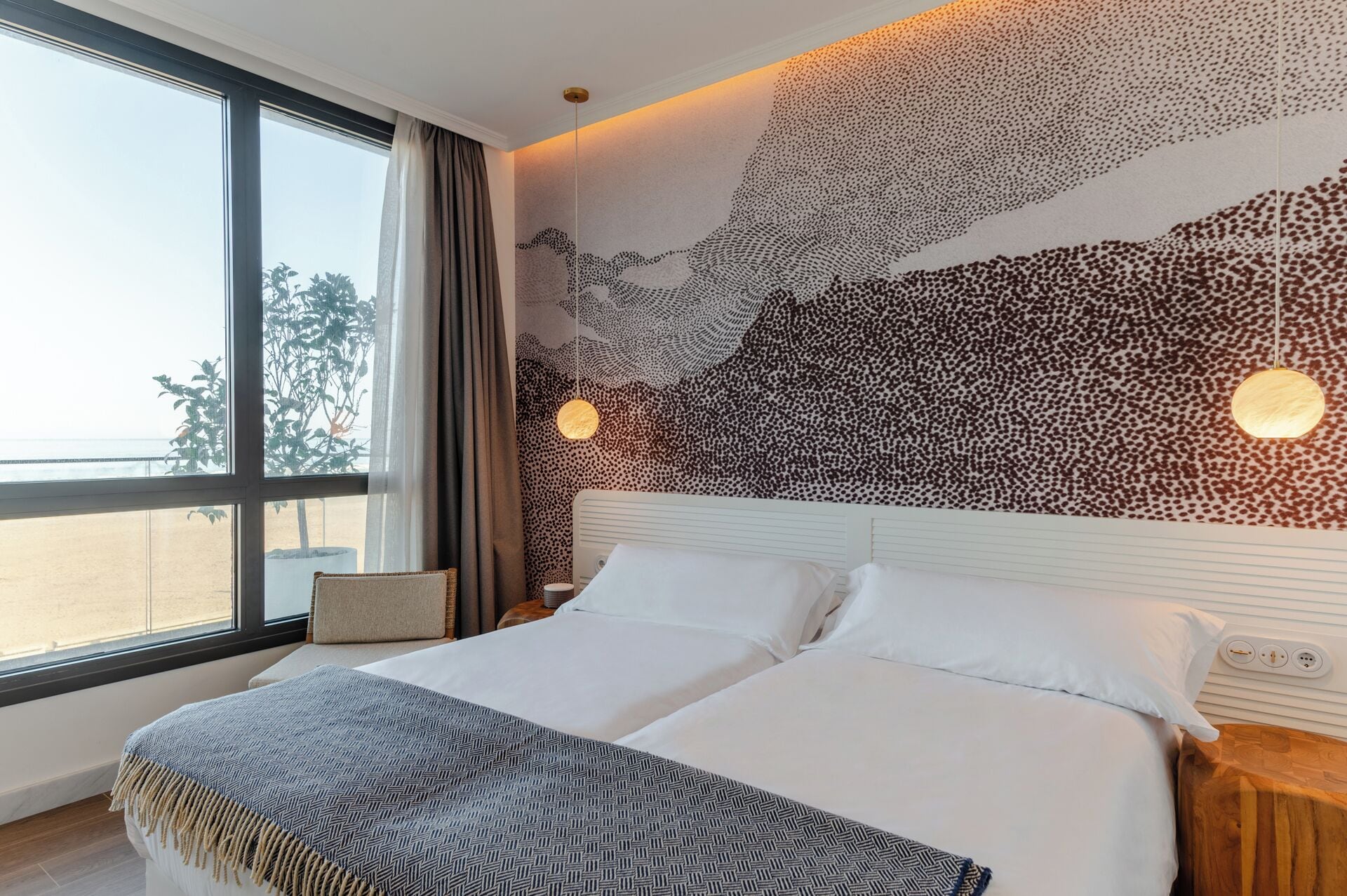 Una habitación de hotel moderna con una cama grande, vista a la playa y un diseño único de arte en la pared.