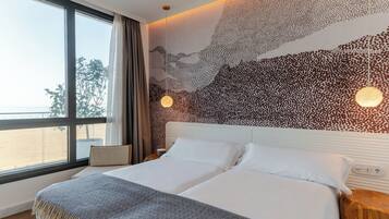 Una habitación de hotel moderna con una cama grande, vista a la playa y un diseño único de arte en la pared.