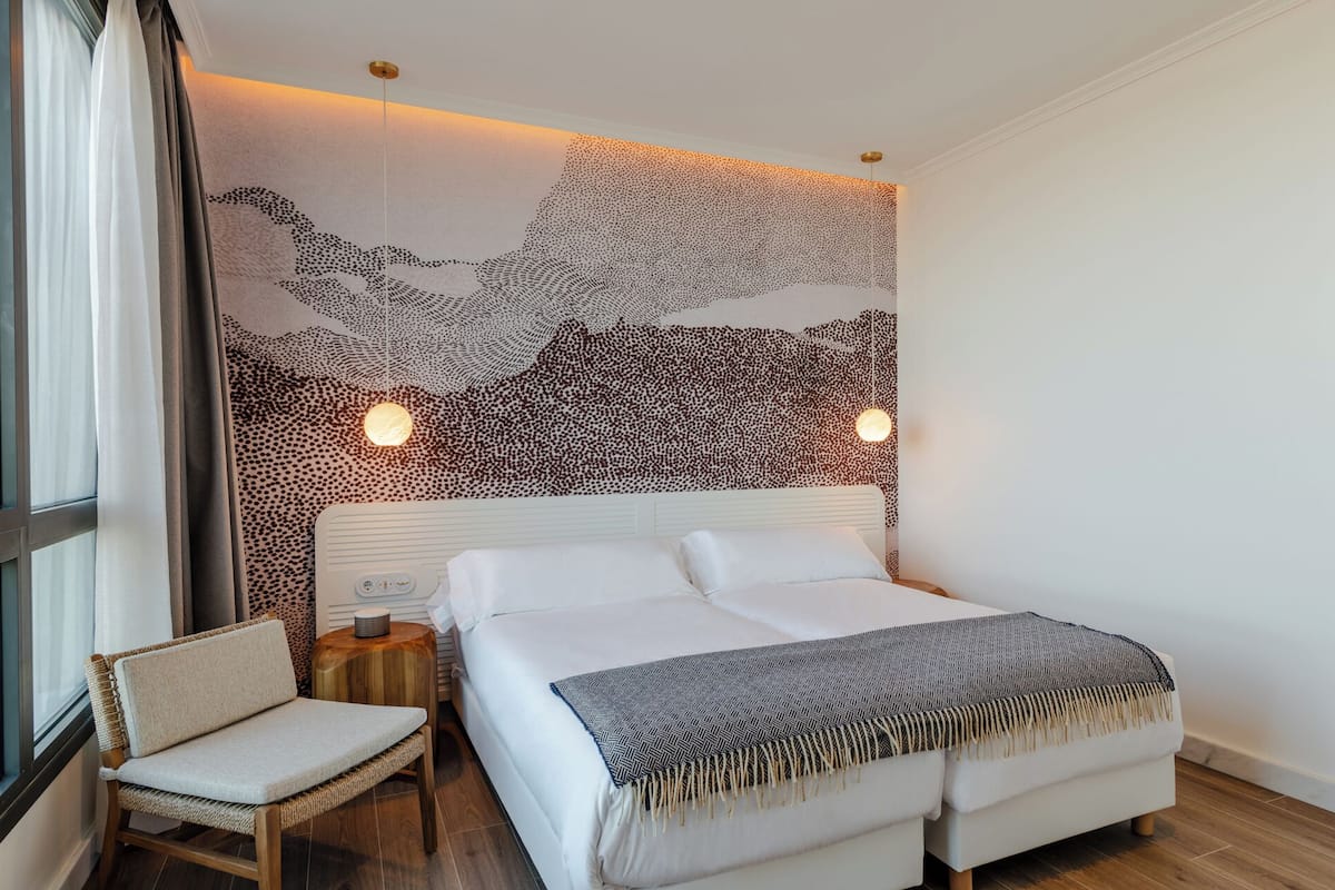 Ein modernes Schlafzimmer mit einem großen Bett, einem Sessel, einem Nachttisch und einer Wand mit strukturierter Oberfläche.