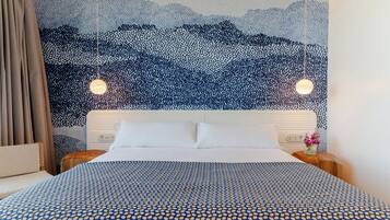 A hotel room with a bed, a headboard, a wall with a dot pattern, and two hanging lights.