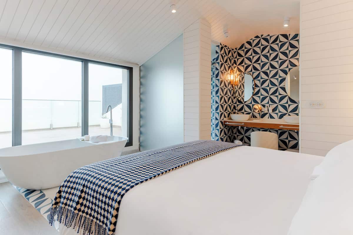 Ein modernes Schlafzimmer mit einem großen Bett, einer integrierten Badewanne und einem Badezimmer mit geometrischen Fliesenmustern.