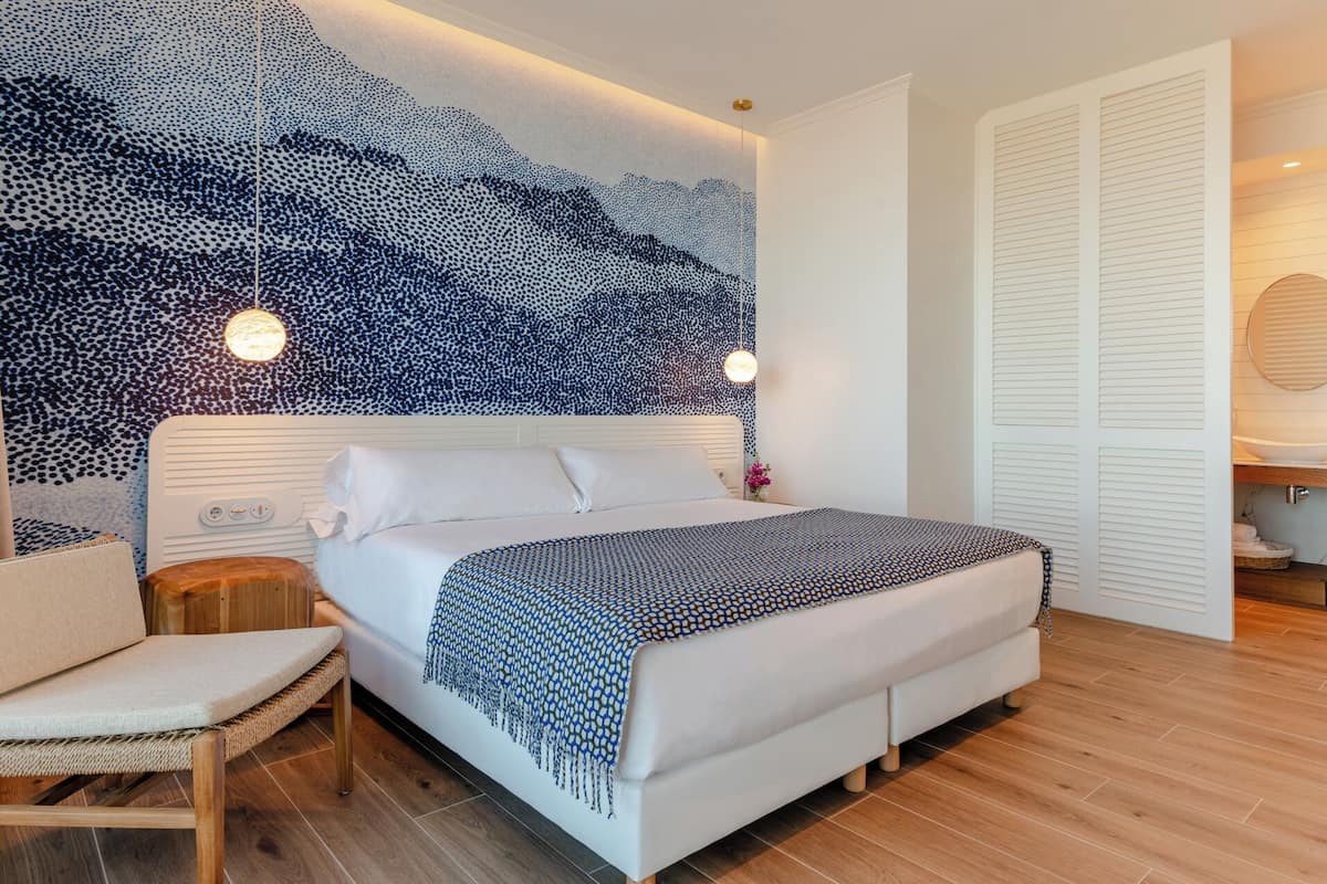 Ein modernes Schlafzimmer mit einem großen Bett, einem Nachttisch, einem Sessel, einer Wand mit blau-weißem Muster und einem weißen Kleiderschrank.