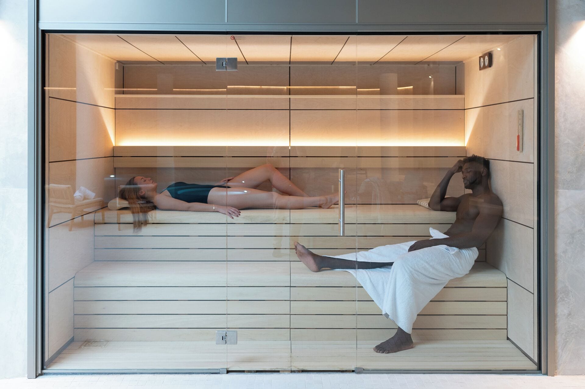 Sauna, jossa on tilaa kahdelle henkilölle, lasiseinä ja puulattia.