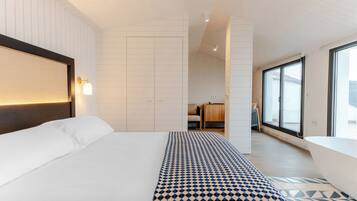 Une chambre d’hôtel moderne avec un grand lit, un tapis à motifs, une tête de lit en bois et une vue dégagée sur l’extérieur grâce à une grande fenêtre.