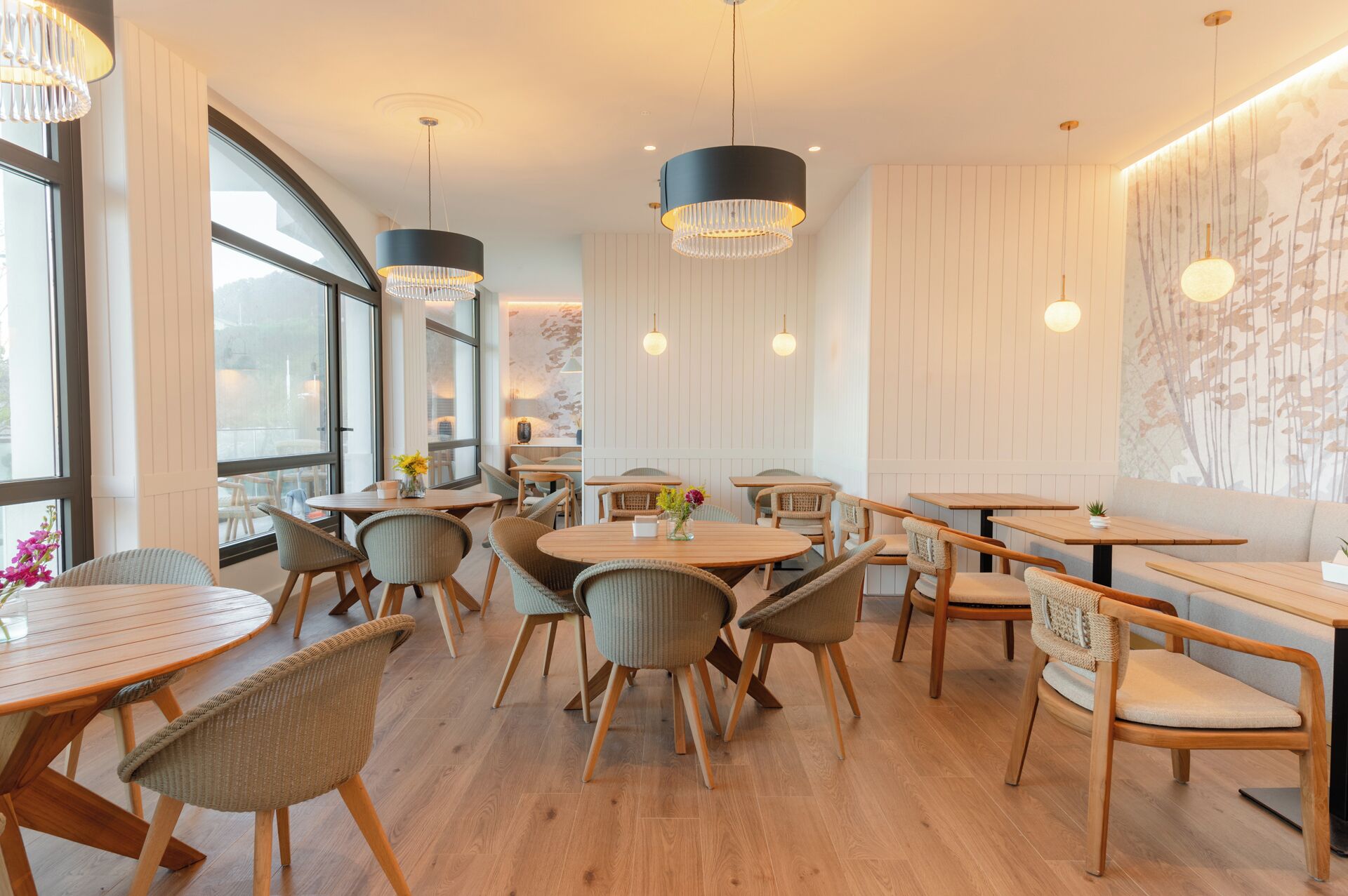 A modern restaurant interior with round tables, wicker chairs, and pendant lighting.