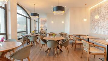 A modern restaurant interior with round tables, wicker chairs, and pendant lighting.