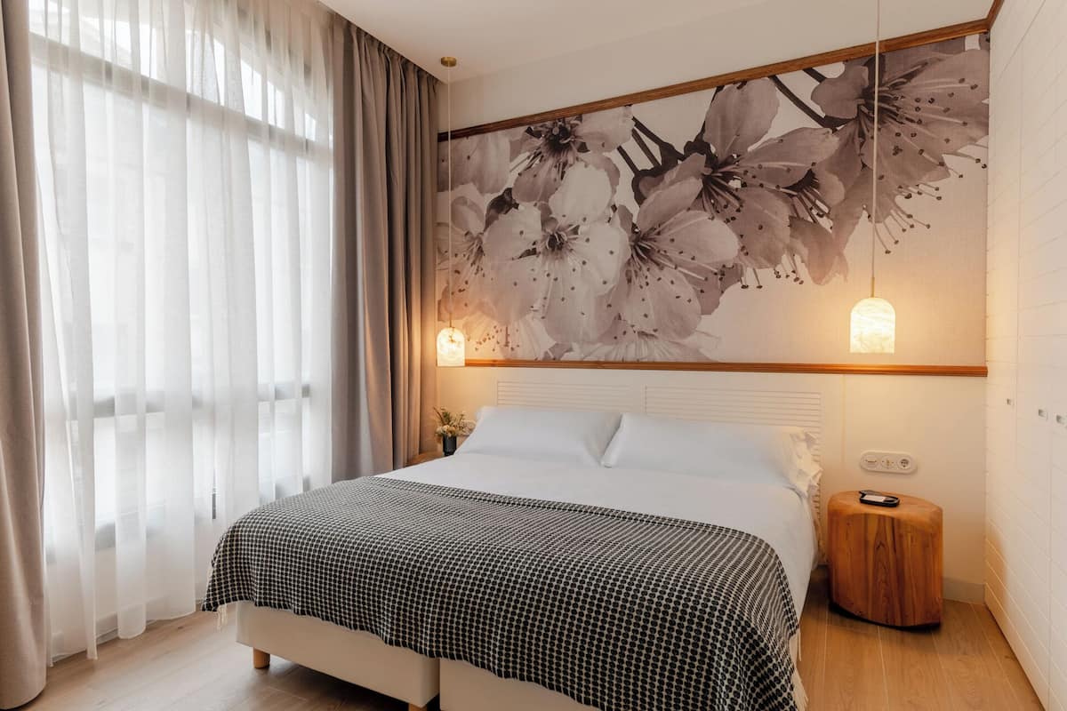 Ein Schlafzimmer mit einem Bett, einer Wandleuchte und einem Blumenbild.