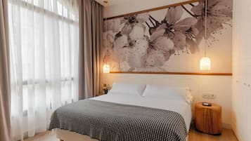 A bedroom with a bed, a wall-mounted light, and a floral artwork.