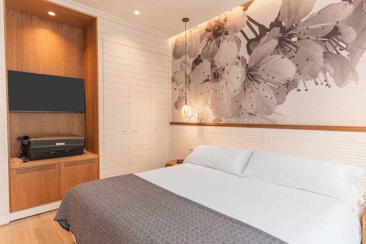 Ein Schlafzimmer mit einem Bett, einem Holzschrank, einem Flachbildfernseher und einer Wandmalerei mit floralem Muster.