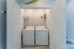 A laundry room with two white front-loading washing machines, a white shelf with laundry baskets and a fire extinguisher.
