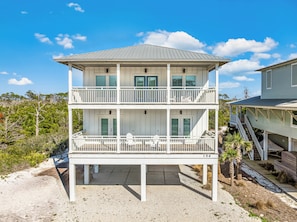 A two-story beachfront house with a balcony, a covered porch, and a staircase leading to the upper level.