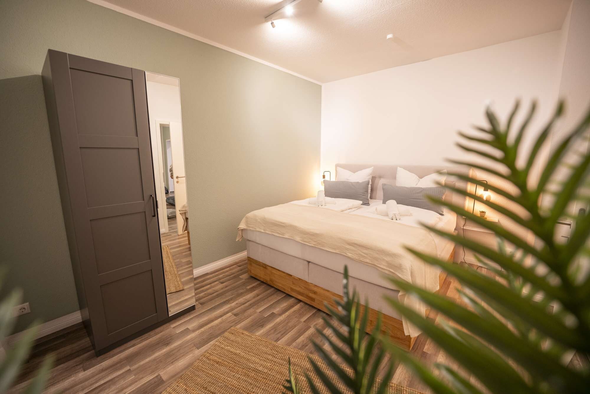 Ein Schlafzimmer mit einem Bett, Nachttischen, einem Spiegel und einer Tür zu einem anderen Raum.