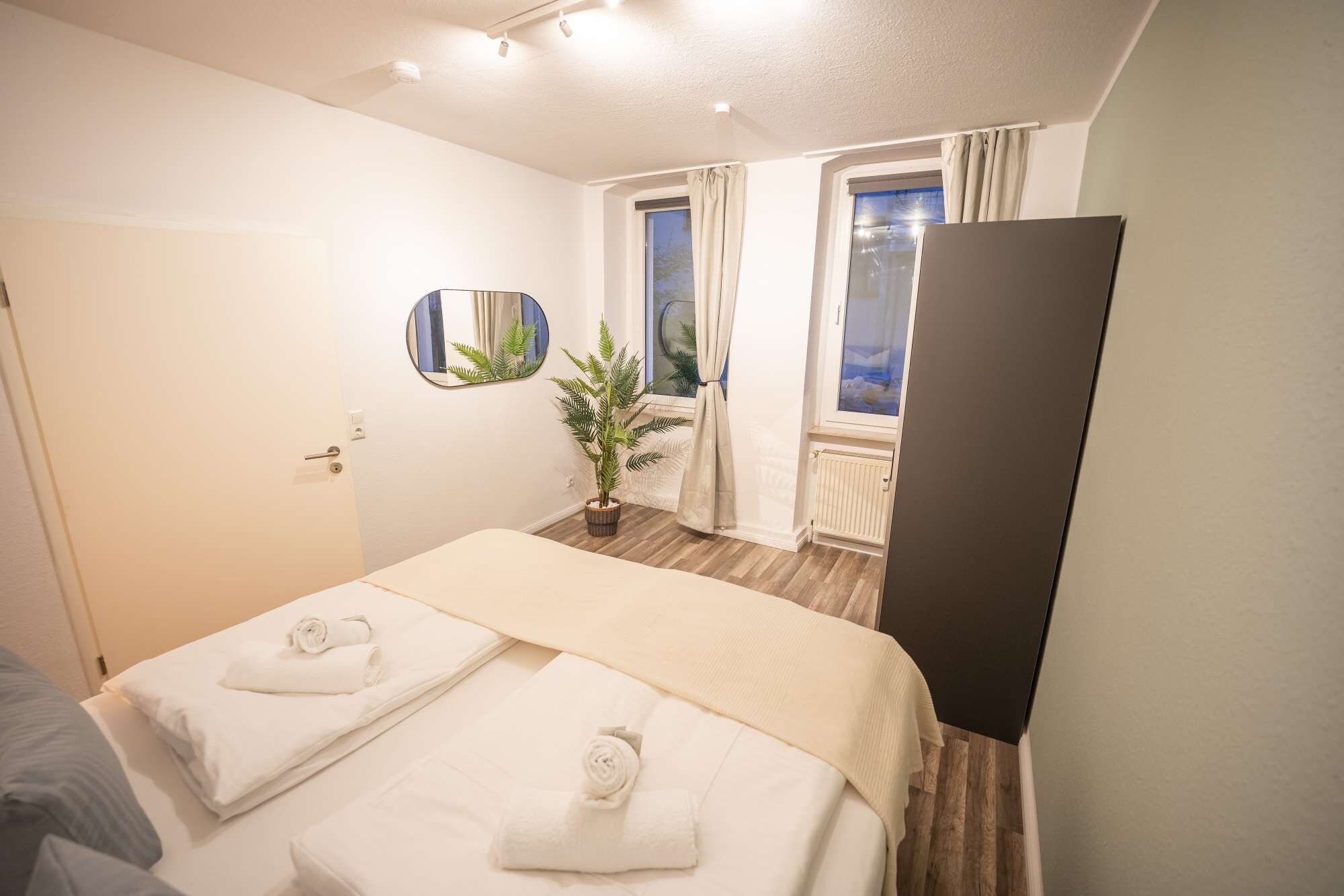 Een hotelkamer met een bed, een spiegel, een potplant en een raam met gordijnen.