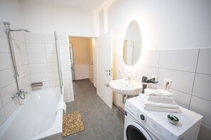 A modern bathroom with a bathtub, a sink, and a washing machine. - RR | Spacious Apt_2-67 m²| Parking | Central (Magdeburg)