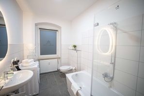 A modern bathroom with a bathtub, a toilet, a sink, and a window. - RR | Spacious Apt_2-67 m²| Parking | Central (Magdeburg)