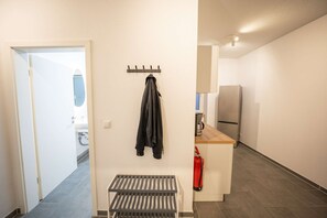 A hallway with a coat rack, a small table, a fire extinguisher, and a kitchen area with a refrigerator. - RR | Spacious Apt_2-67 m²| Parking | Central (Magdeburg)