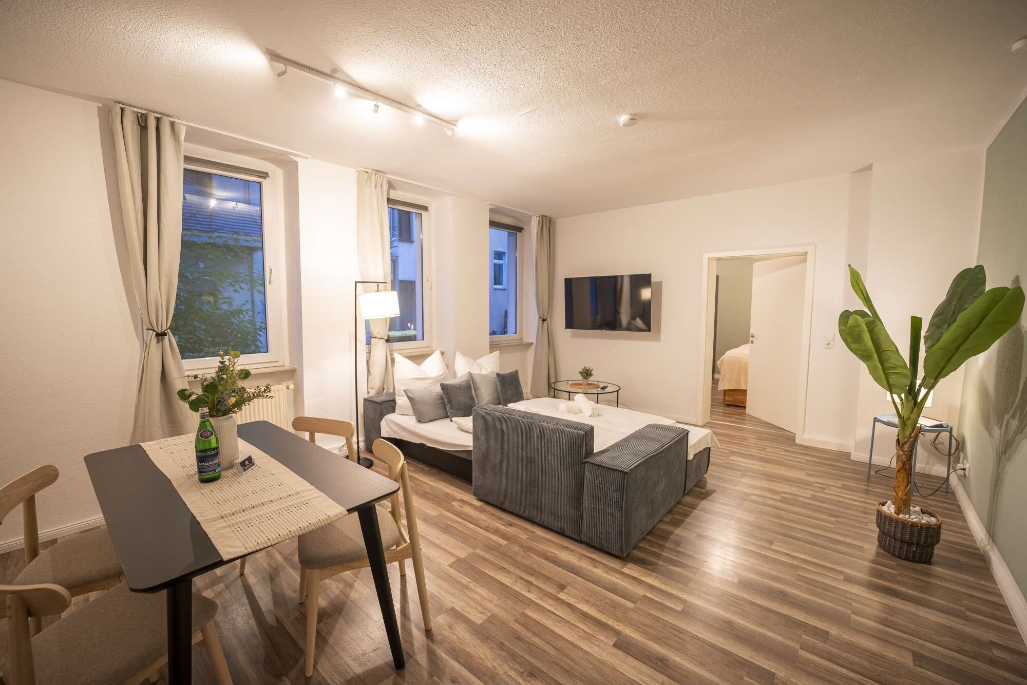 Een moderne woonkamer met een eethoek, een zithoek, een salontafel en een potplant.